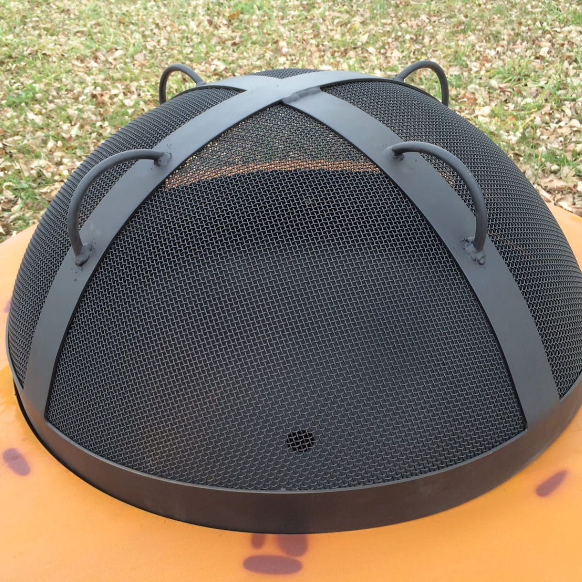27.5” black heavy stainless steel mesh Spark Guard with two-inch wide 304 stainless steel bands sitting on fire pit. Fits Fire Pit Art style: Saturn (sold separately). Made in America.