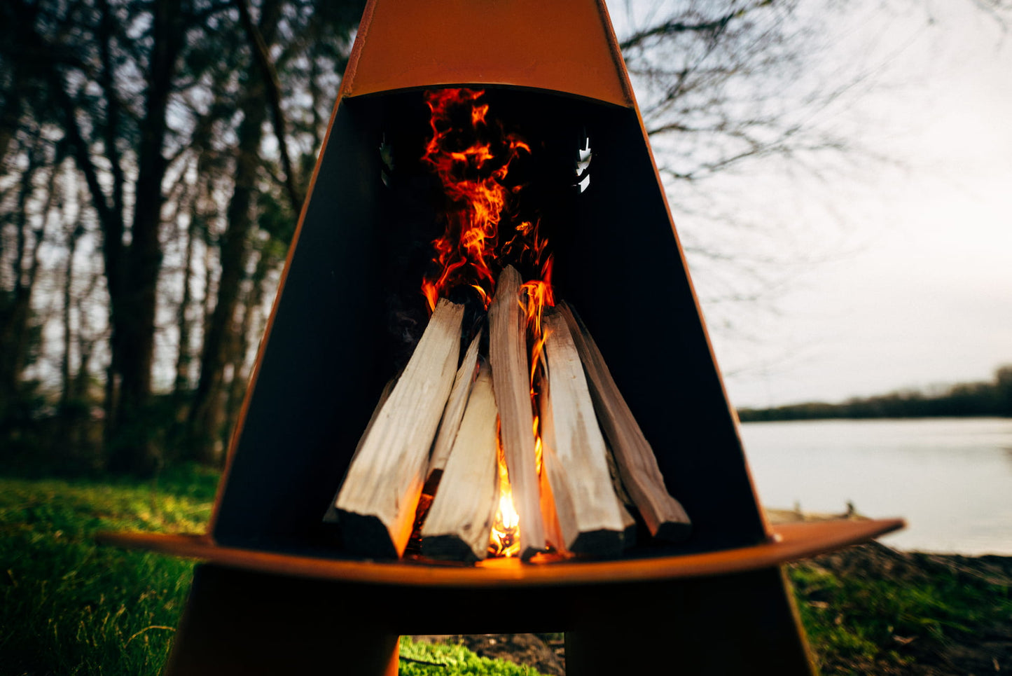 Wooden teepee-style fire pit with flames in a natural setting
