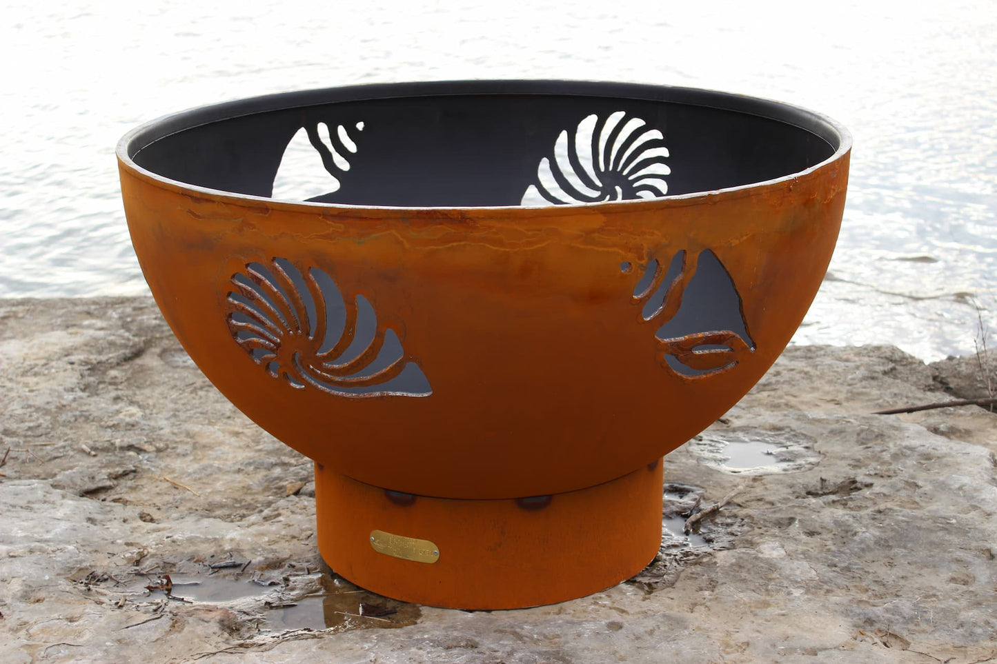 Full view of Fire Pit Art's Beachcomber 36" steel fire pit showing shell and conch designs in daylight.