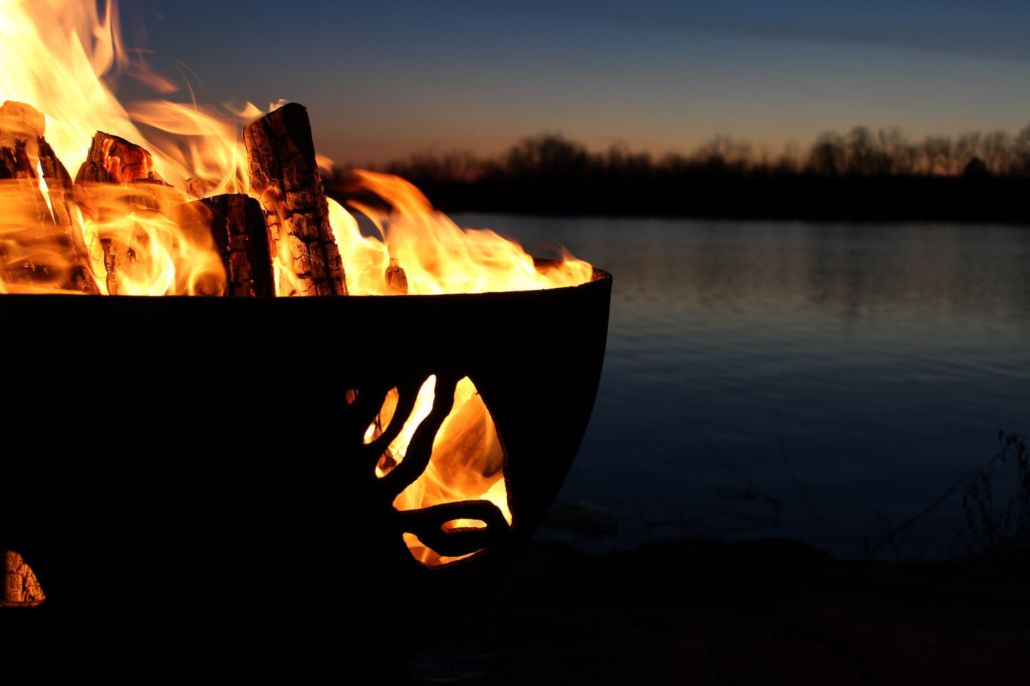 Fire burning in Beachcomber 36" steel fire pit near water's edge at night. Made by Fire Pit Art.