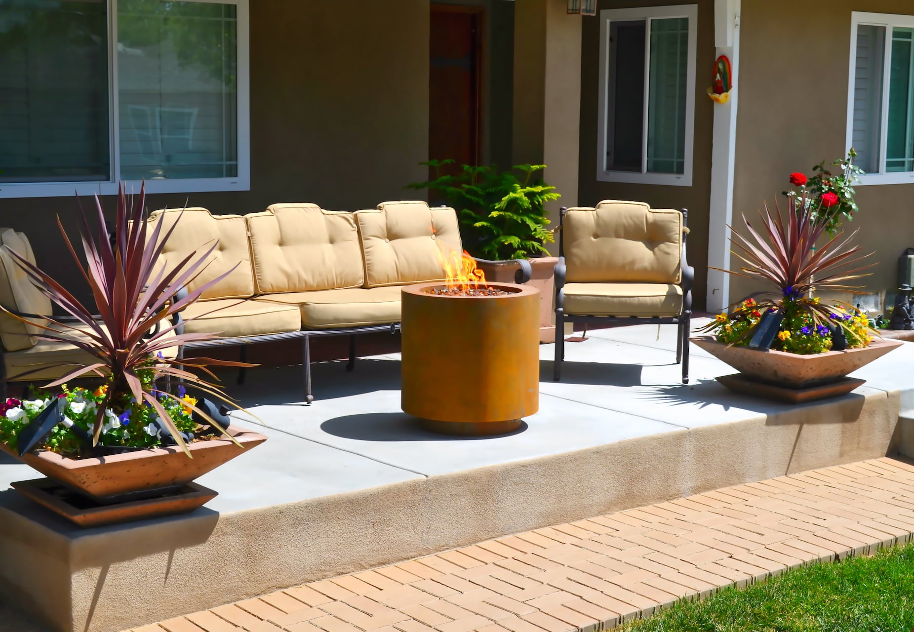 Beverly Corten Steel Propane Fire Pit on a patio with tan seating and decorative planters.