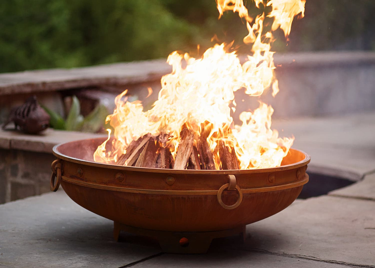 Side view of Fire Pit Art's Emperor 37" carbon steel fire pit showing rounded bowl shape with glowing firewood. Made in USA.