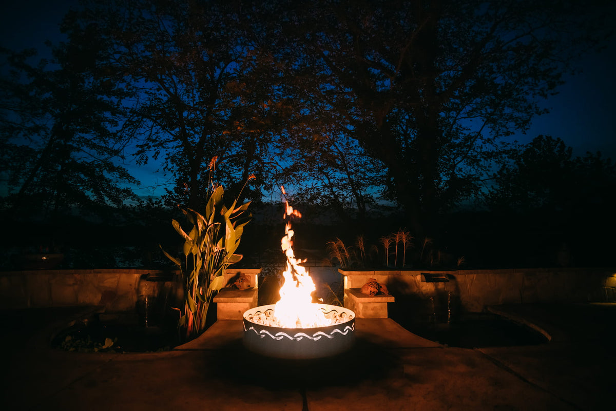 Fire Surfer fire pit glowing at dusk on stone patio by garden.