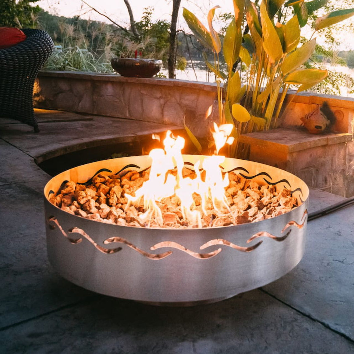 Fire Surfer steel fire pit with bright flame on patio at sunset. Made in the USA by Fire Pit Art.
