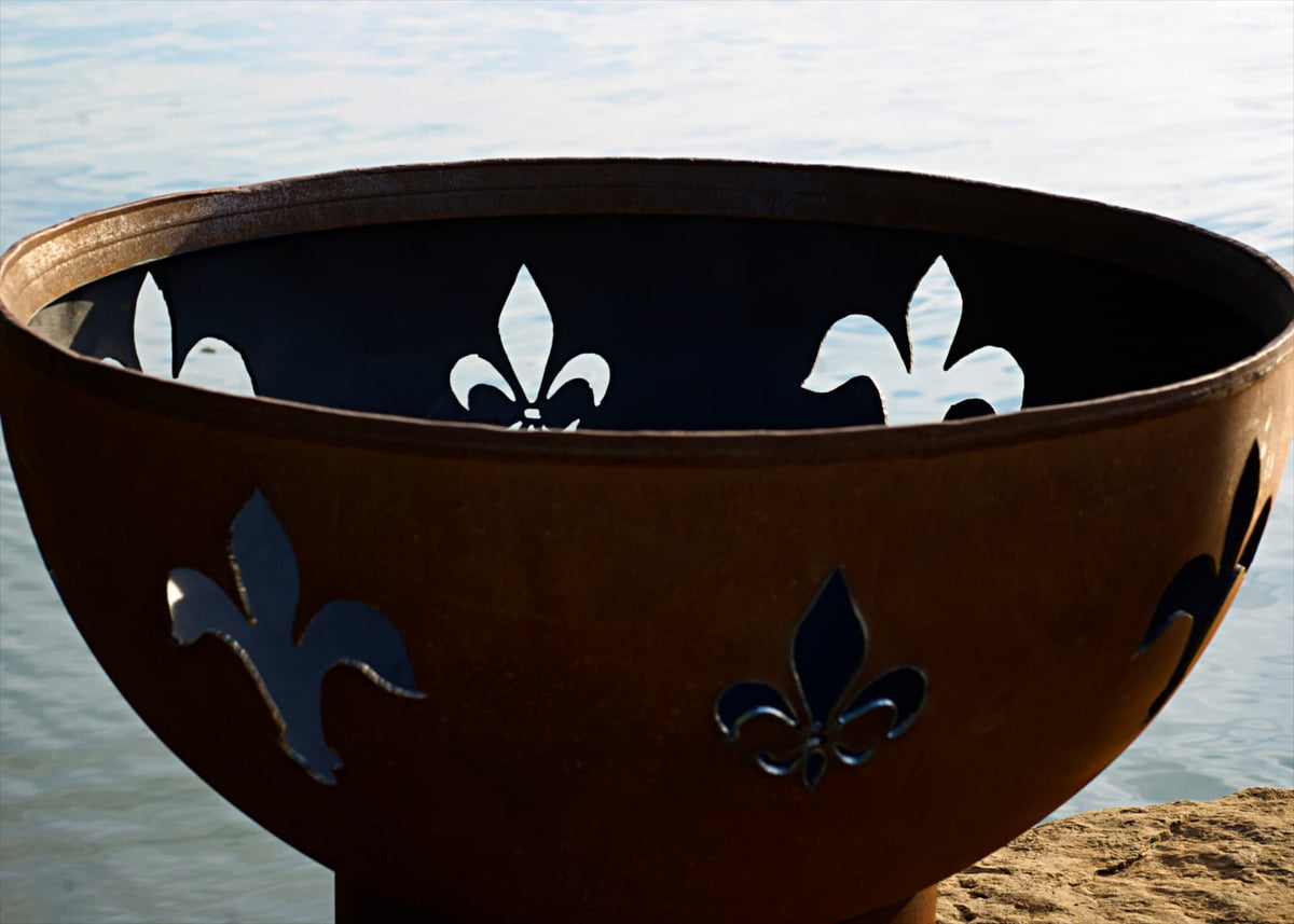 Decorative fire pit with fleur-de-lis patterns against a water background. Made in the USA of carbon steel.