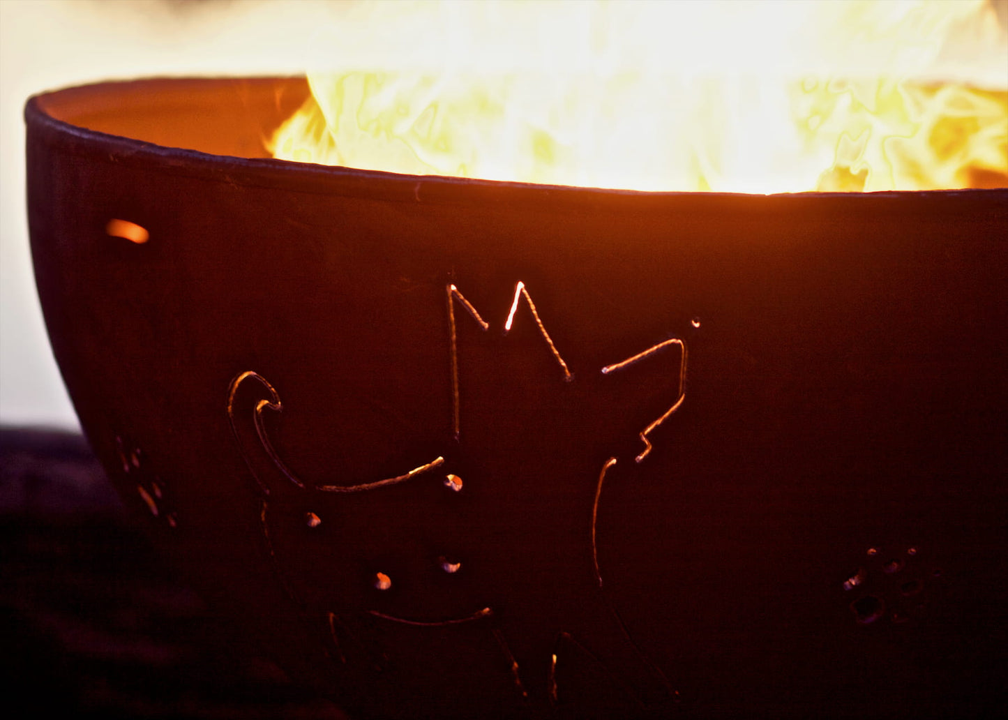 Closeup of Fire Pit Art's Funky Dog carbon steel fire pit showing dog silhouette and paw print cutouts with warm glow from fire.