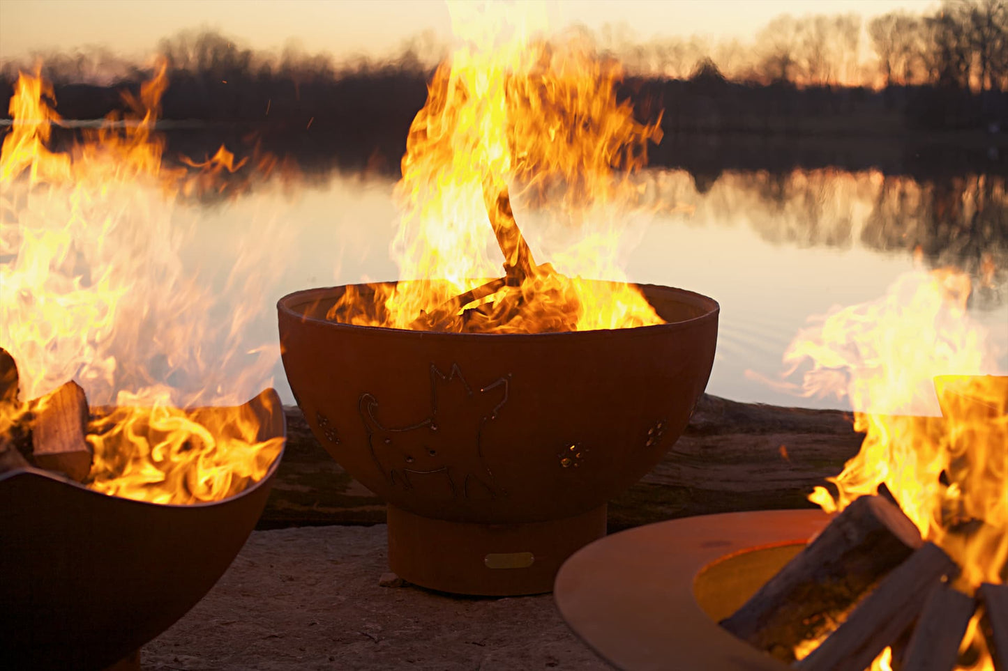 Funky Dog 36" carbon steel fire pit lit alongside other fire pits, showing playful design and ambiance at sunset. Made in the USA by Fire Pit Art.