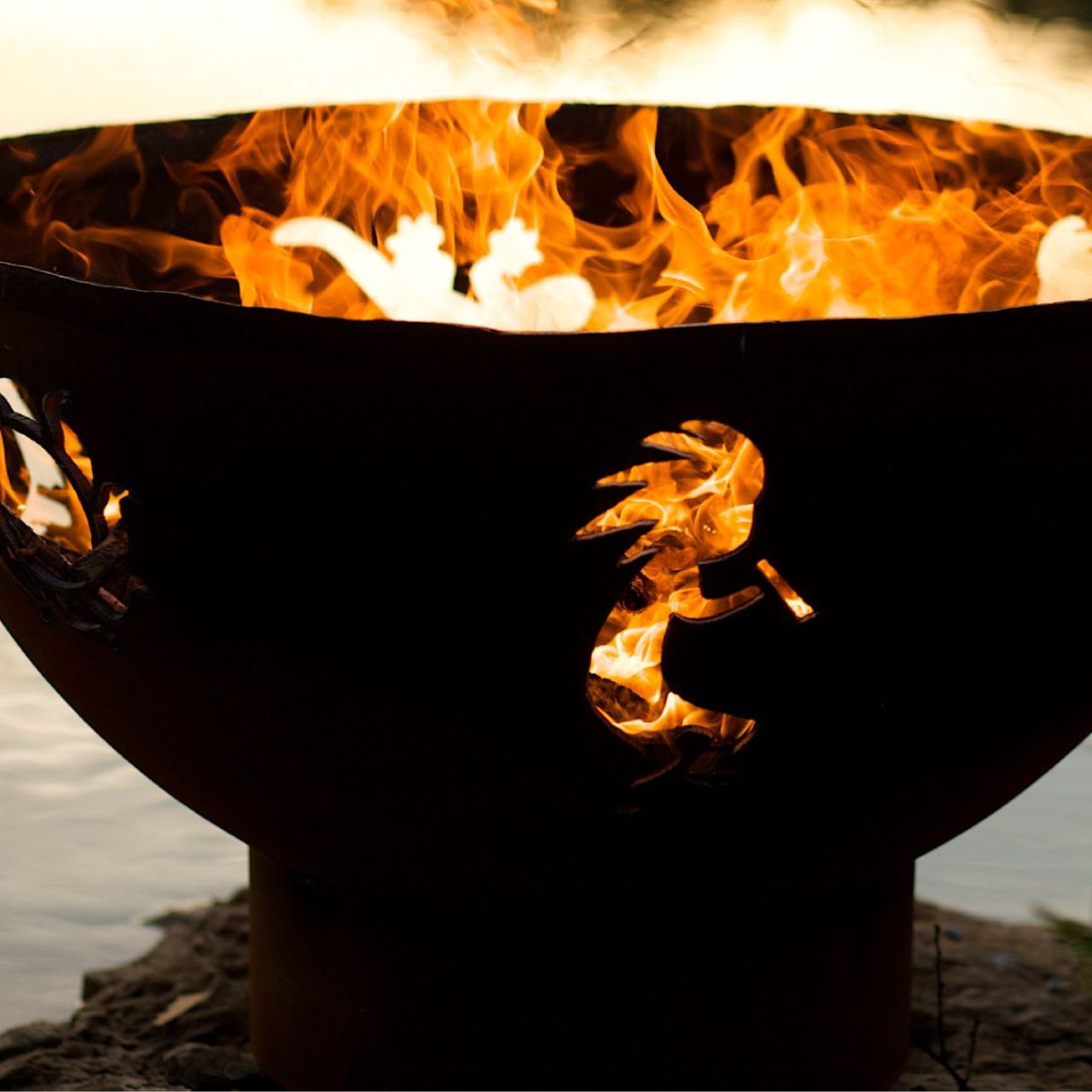 Fire Pit Art's Kokopelli 36" carbon steel fire pit with flames emerging through sunburst and Kokopelli cutouts.