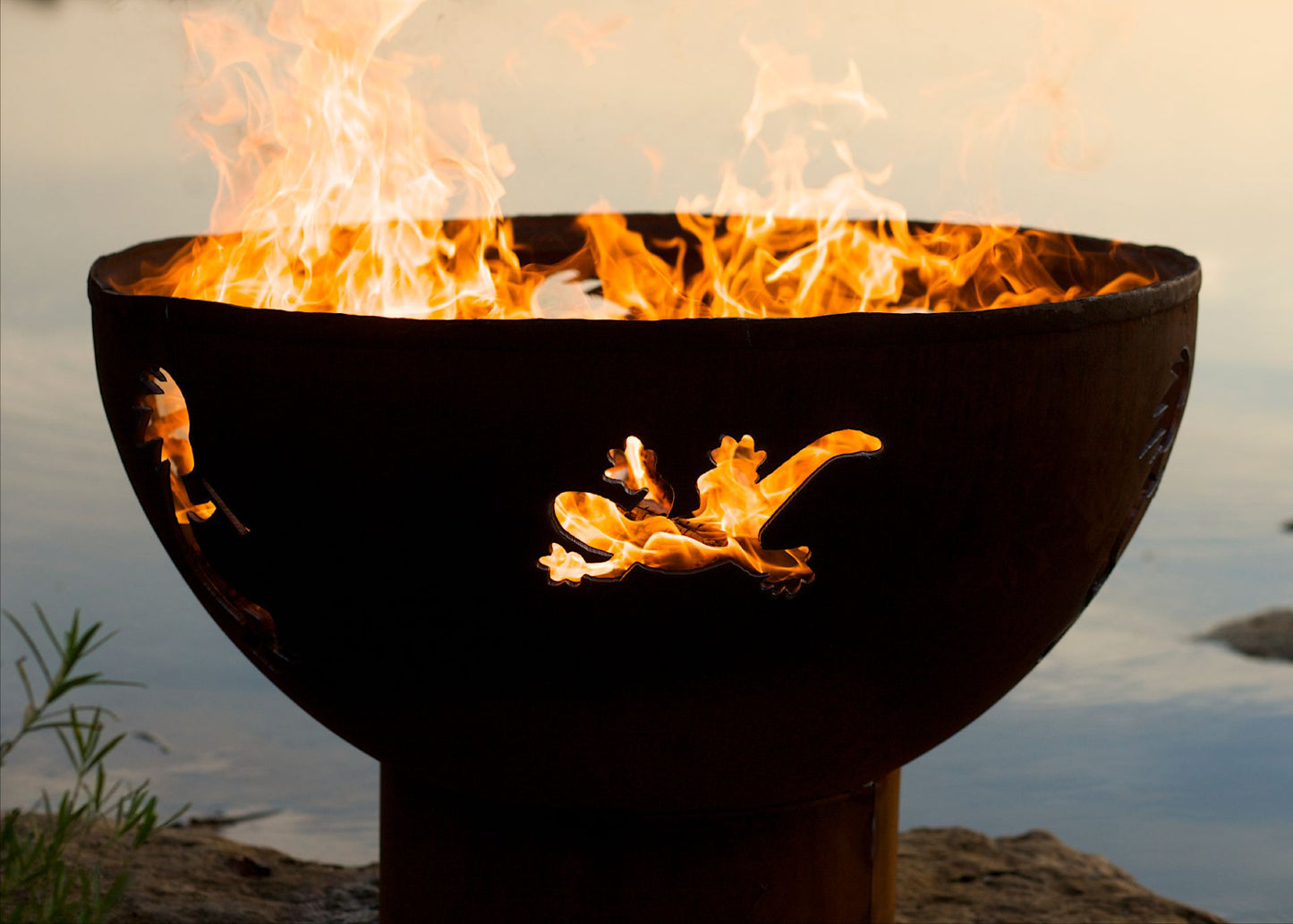 Lakeside Kokopelli 36" carbon steel fire pit with gecko design glowing with fire.