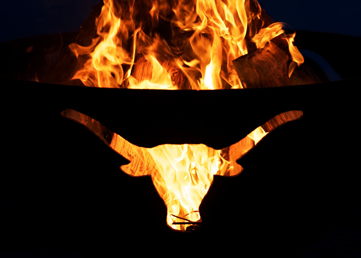 Close view of fire flickering through longhorn cutout in Long Horn 36" carbon steel fire pit. Made in USA.