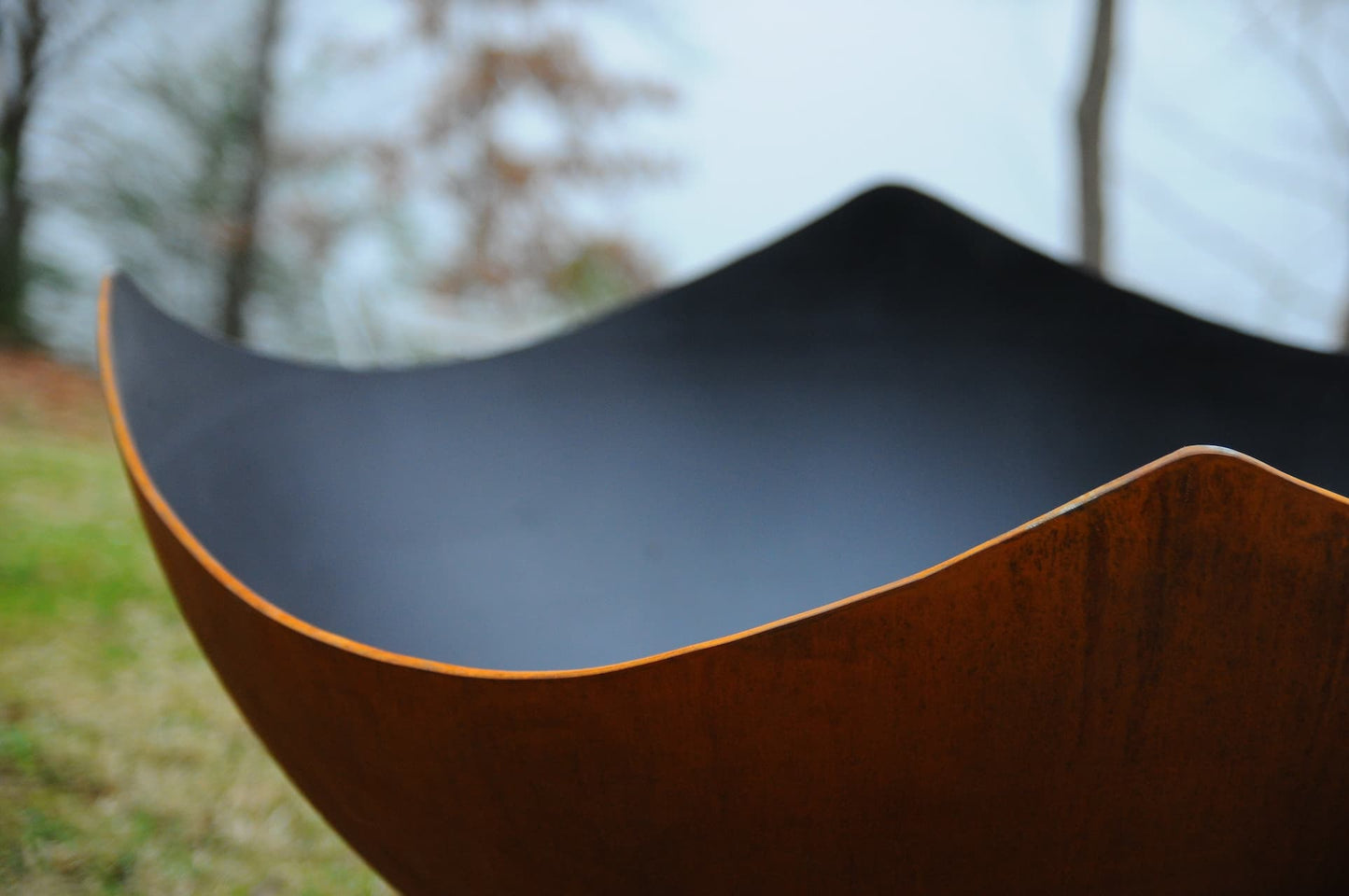 Close-up of the inside of an unlit Manta Ray 36" carbon steel fire pit with blurred background.