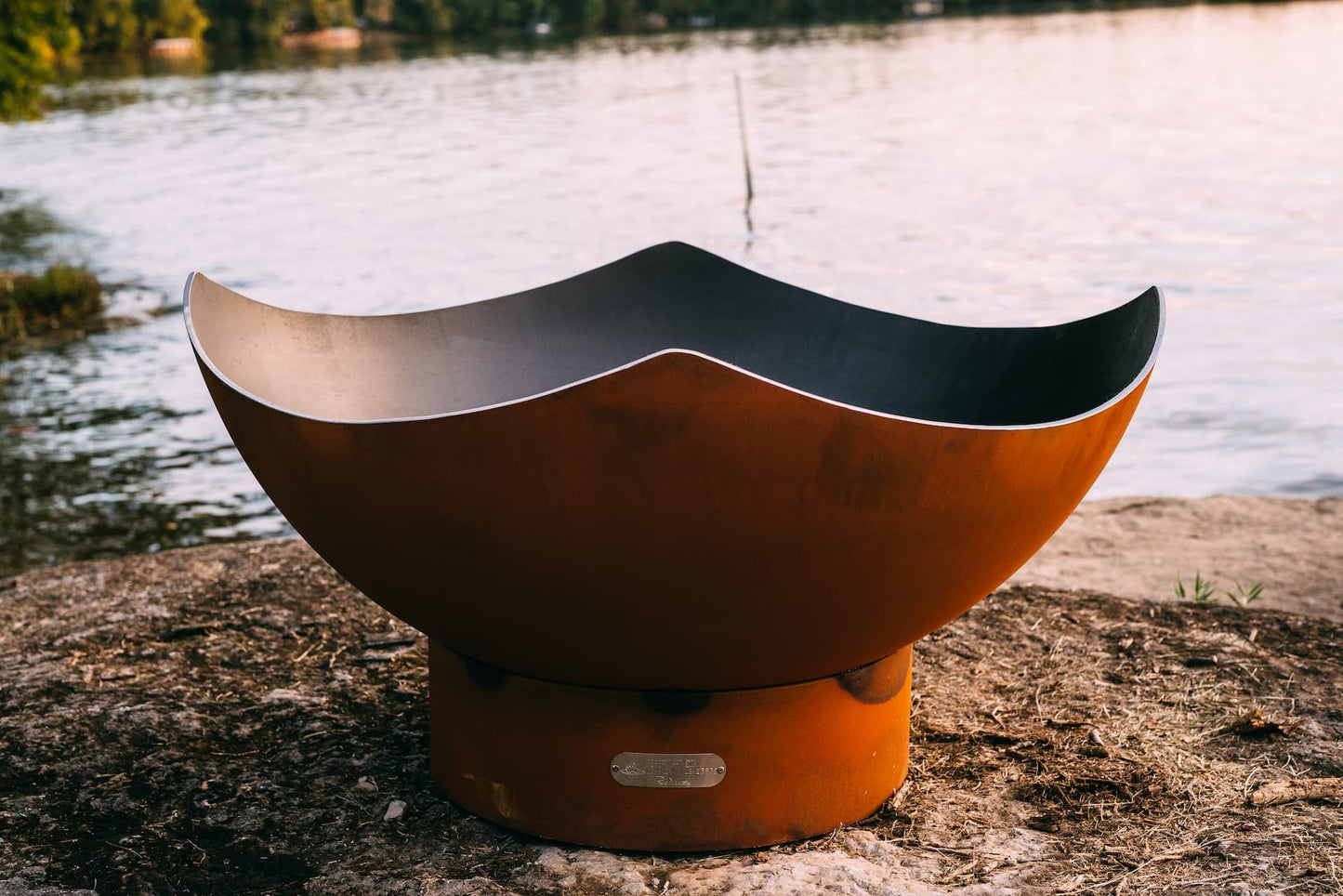 Close-up of inside the Manta Ray fire pit with curved steel edges by a lake.