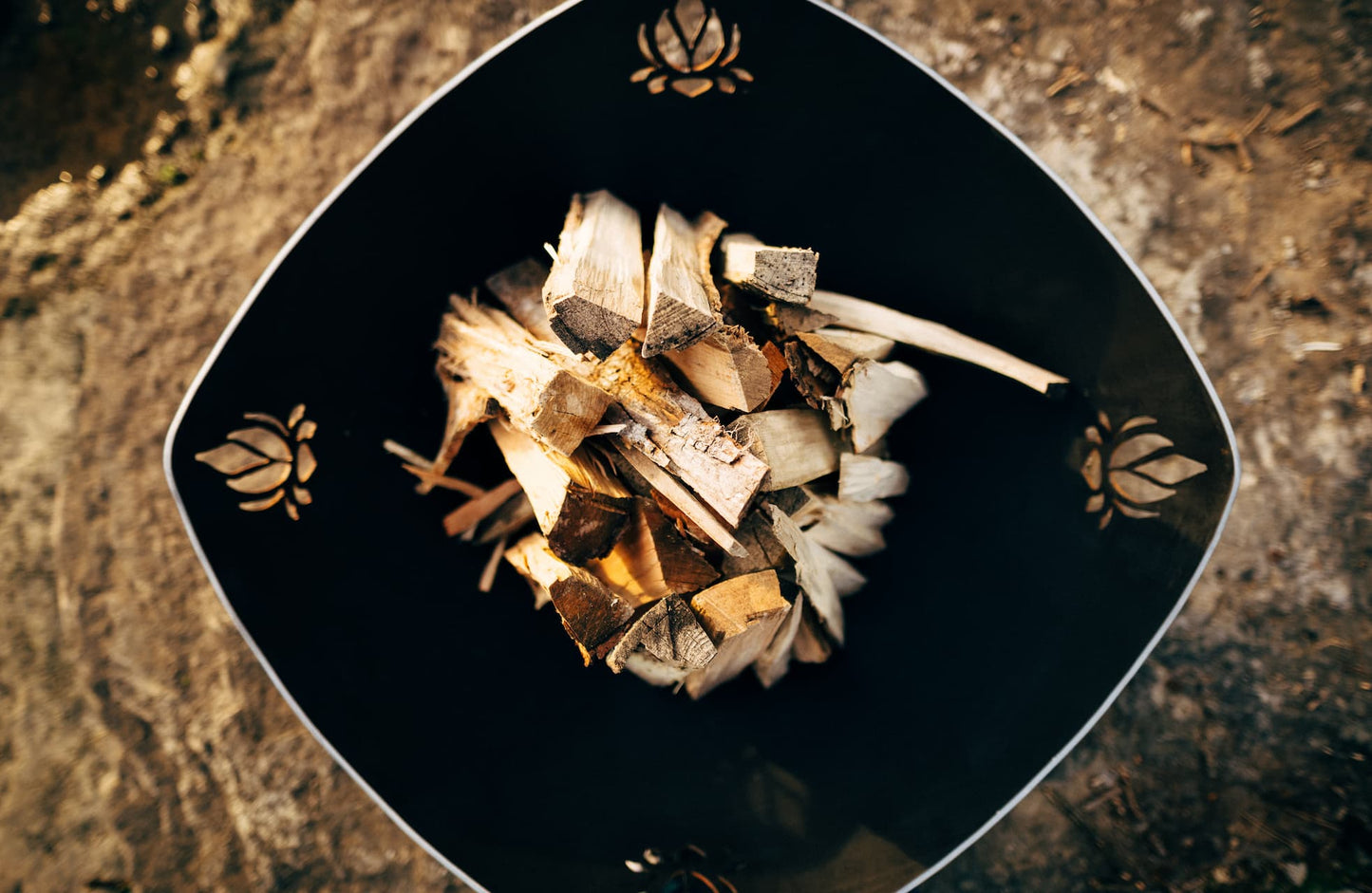 Topview of Namaste' 36" fire pit. Has unlit wood inside with view of all four Lotus Flower cutouts.