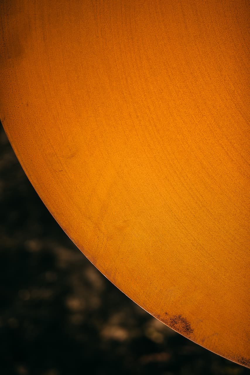 Close-up of the Saturn fire pit lid showing the natural steel patina finish and subtle texture detail on the wide outer ring.