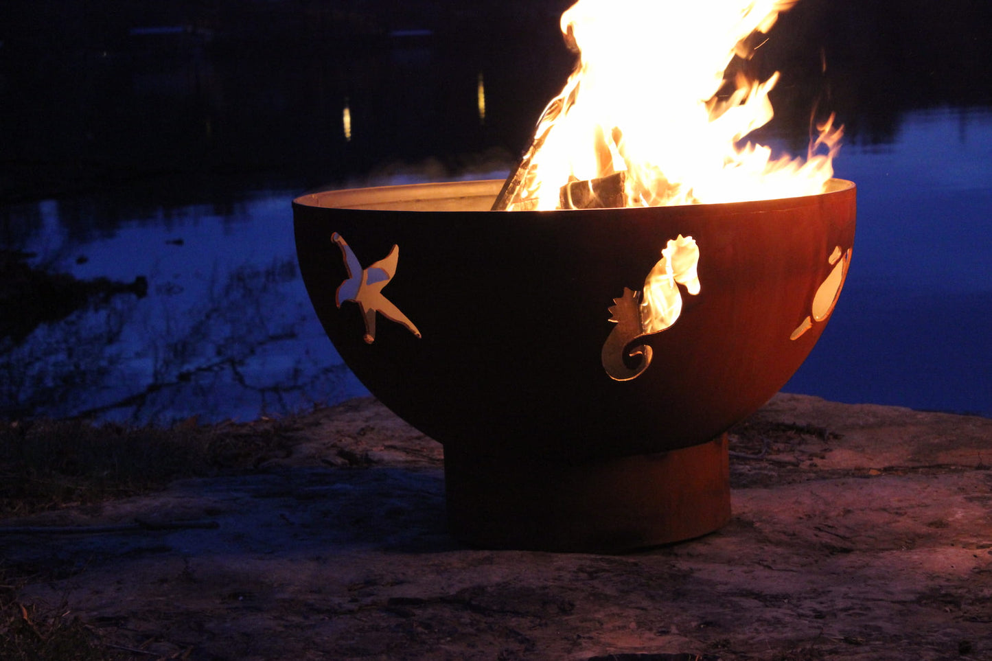 Sea Creatures fire pit at night with bright flame and seahorse, starfish, and turtle designs.