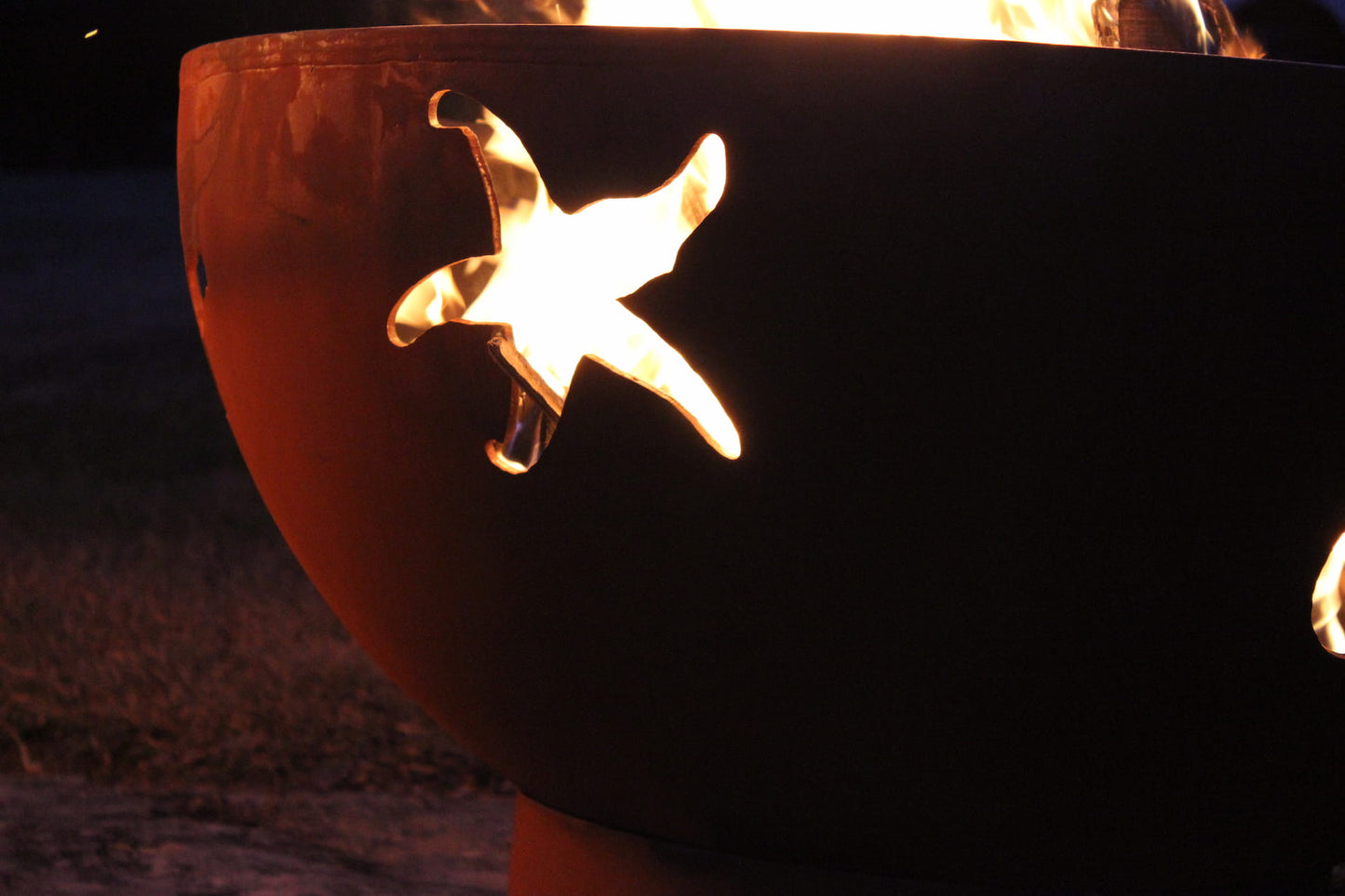 Close-up of starfish cutout illuminated by firelight on the Sea Creatures 36" carbon steel fire pit.