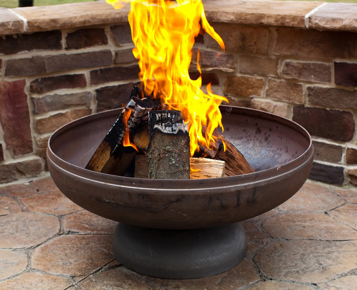 The Patriot fire pit with roaring flame against a brick wall backdrop.