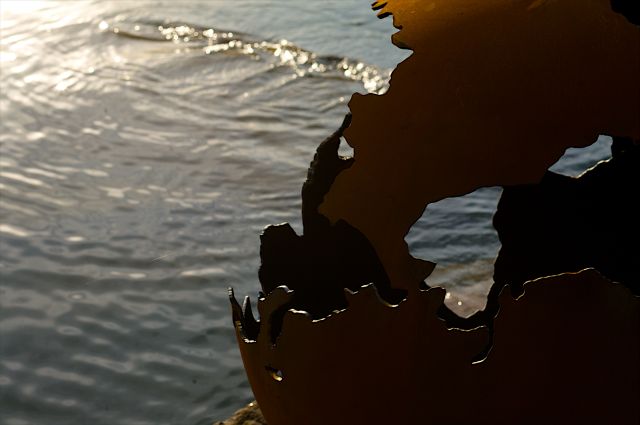 Silhouette of Fire Pit Art's Third Rock 36" carbon steel fire pit against water.