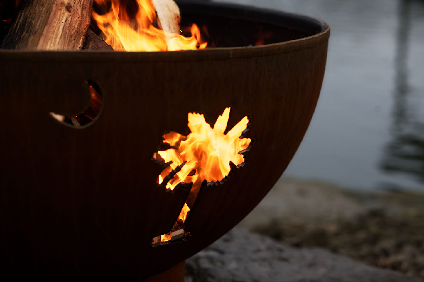 Flames glowing through the palm tree cutout of the Tropical Moon 36" carbon steel fire pit with the crescent cutout visible above.