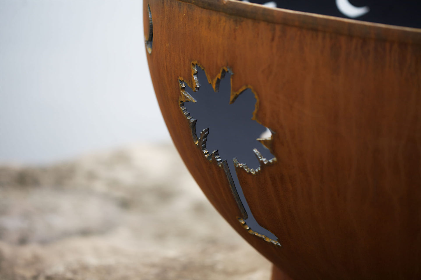 Close-up of the palm tree cutout on the Tropical Moon steel fire pit, showing the raw steel edge and weathered patina.