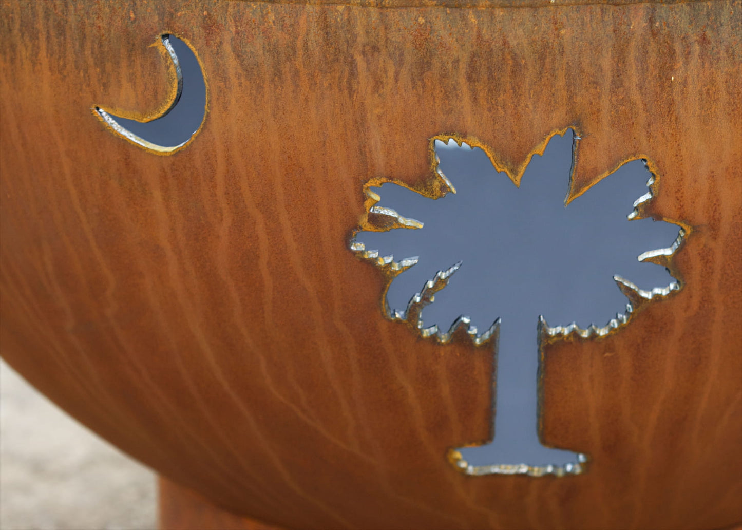 Detailed view of the crescent moon and palm tree cutouts on the Tropical Moon 36-inch carbon steel fire pit by Fire Pit Art.