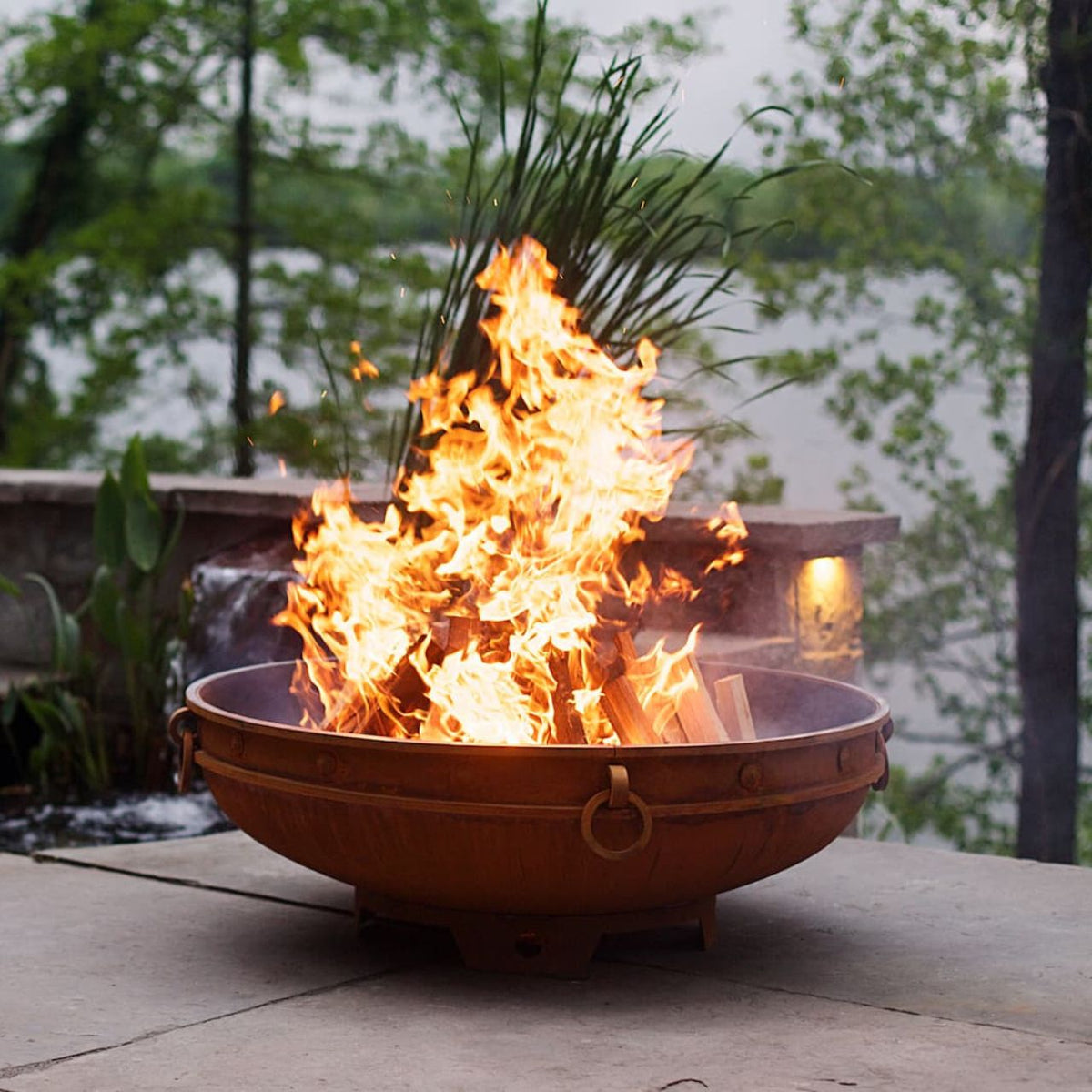 Brown Circular Wood Burning Fire Pit on Brick Patio.