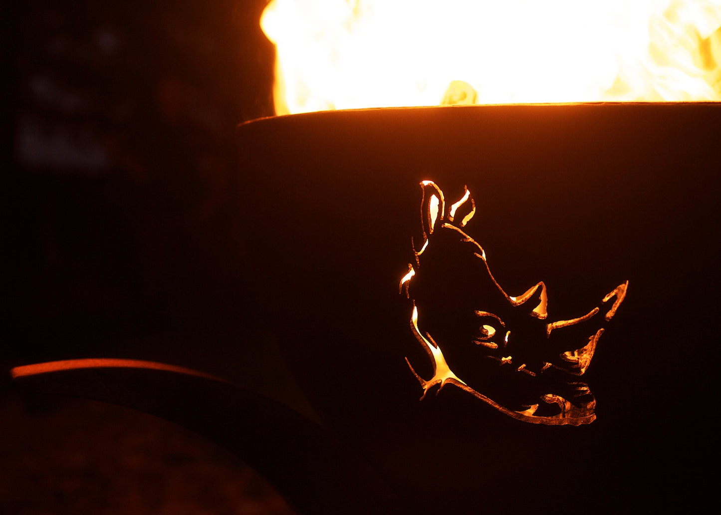 Night fire in carbon steel fire pit with glowing rhino silhouette.