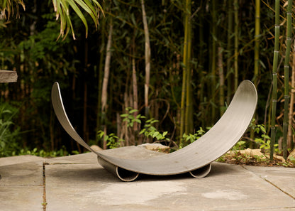 Sideview of Fire Pit Art’s stainless steel crescent-shaped log rack on patio.