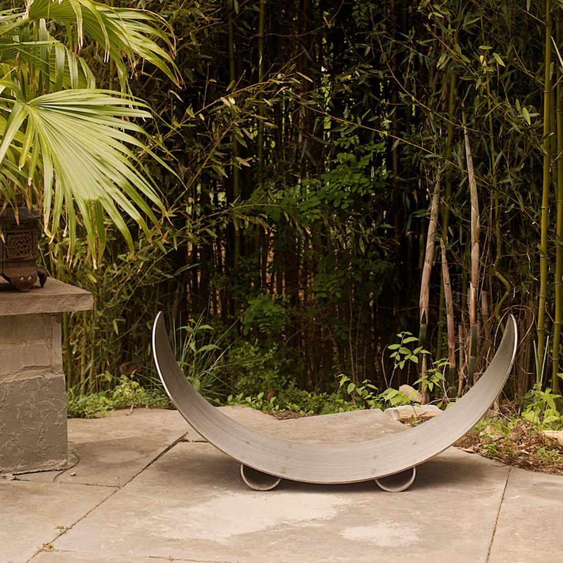 Sideview of Fire Pit Art’s stainless steel crescent-shaped log rack on patio.