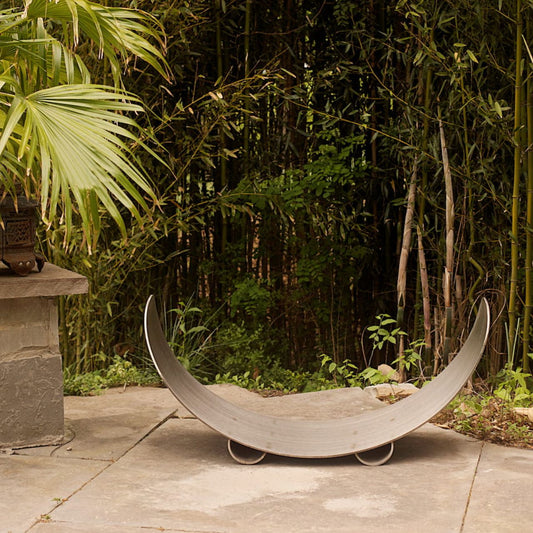 Sideview of Fire Pit Art’s stainless steel crescent-shaped log rack on patio.