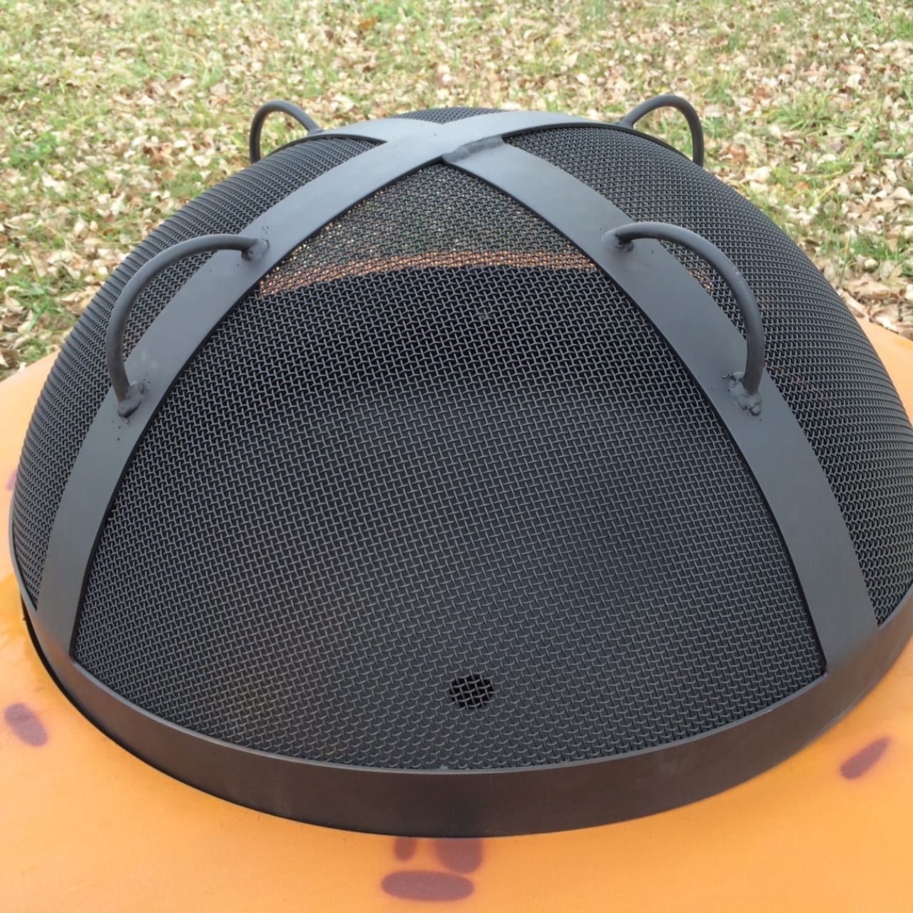 27.5” black heavy stainless steel mesh Spark Guard with two-inch wide 304 stainless steel bands sitting on fire pit.  Fits Fire Pit Art style: Saturn (sold separately).  Made in America.
