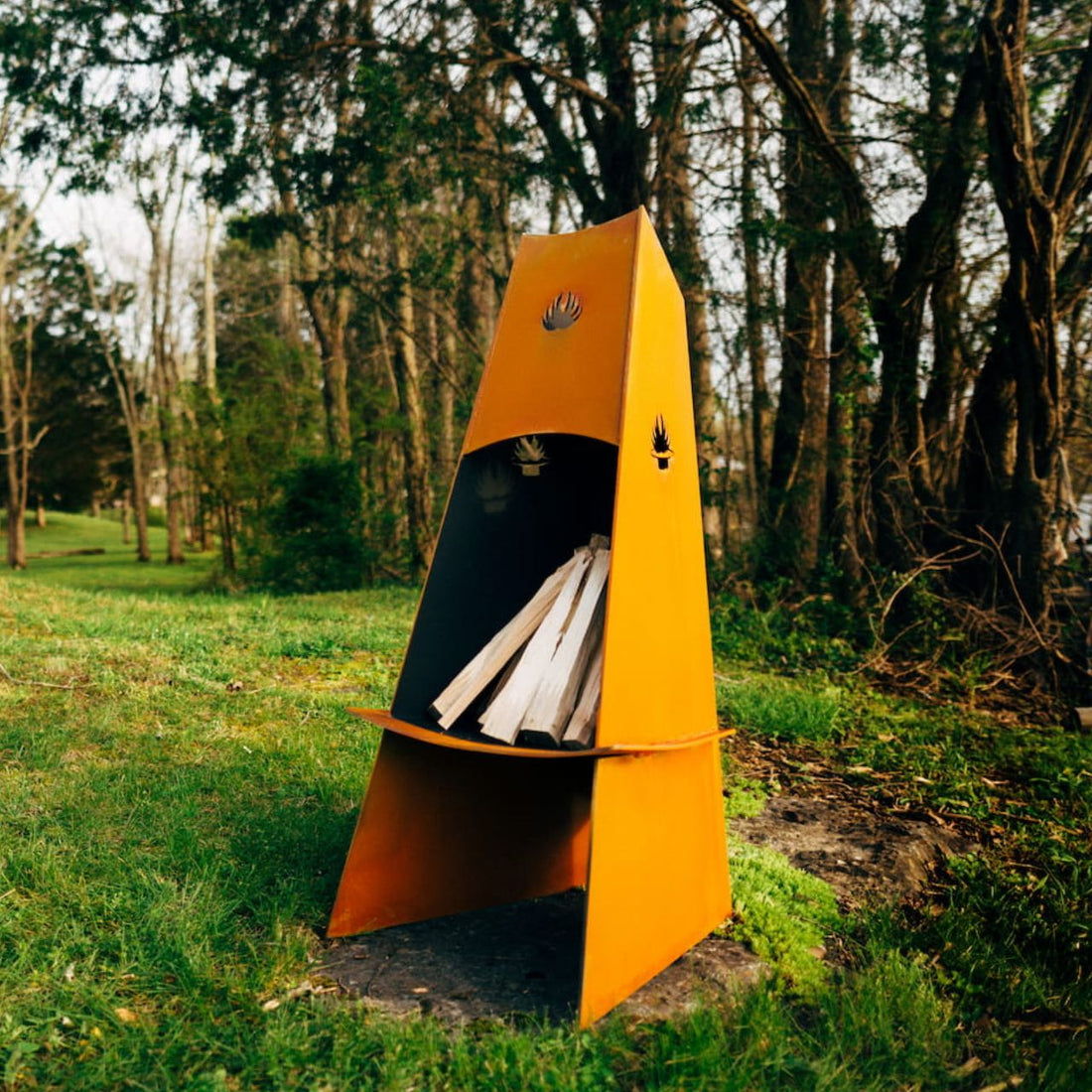 Vesuvius wood-burning fire pit by Fire Pit Art—corten steel chiminea with stacked logs in a backyard setting.