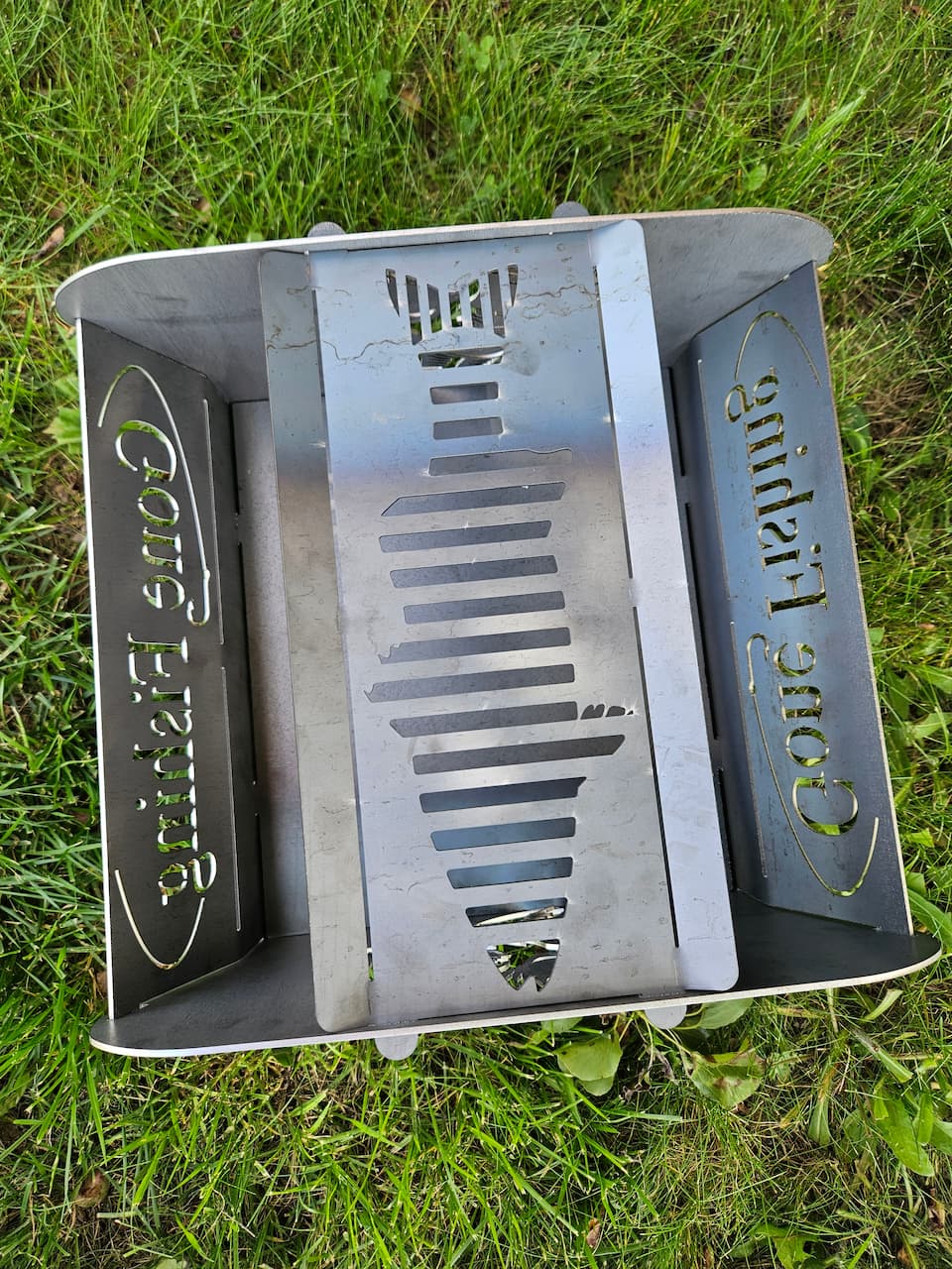 Overhead view of Gone Fishing steel collapsible fire pit with cut out of a fish to use for grilling.