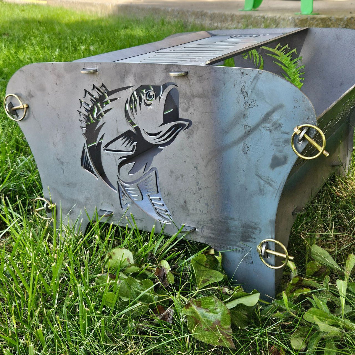 A portable collapsible steel fire pit with a fish design on one side and the words &