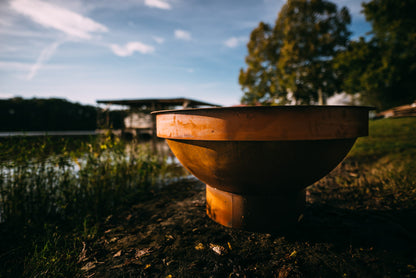 Sideview of fire pit next to lake.  The fire pit has a Fire Pit Art 43” Carbon Steel Table Top Lid covering it.