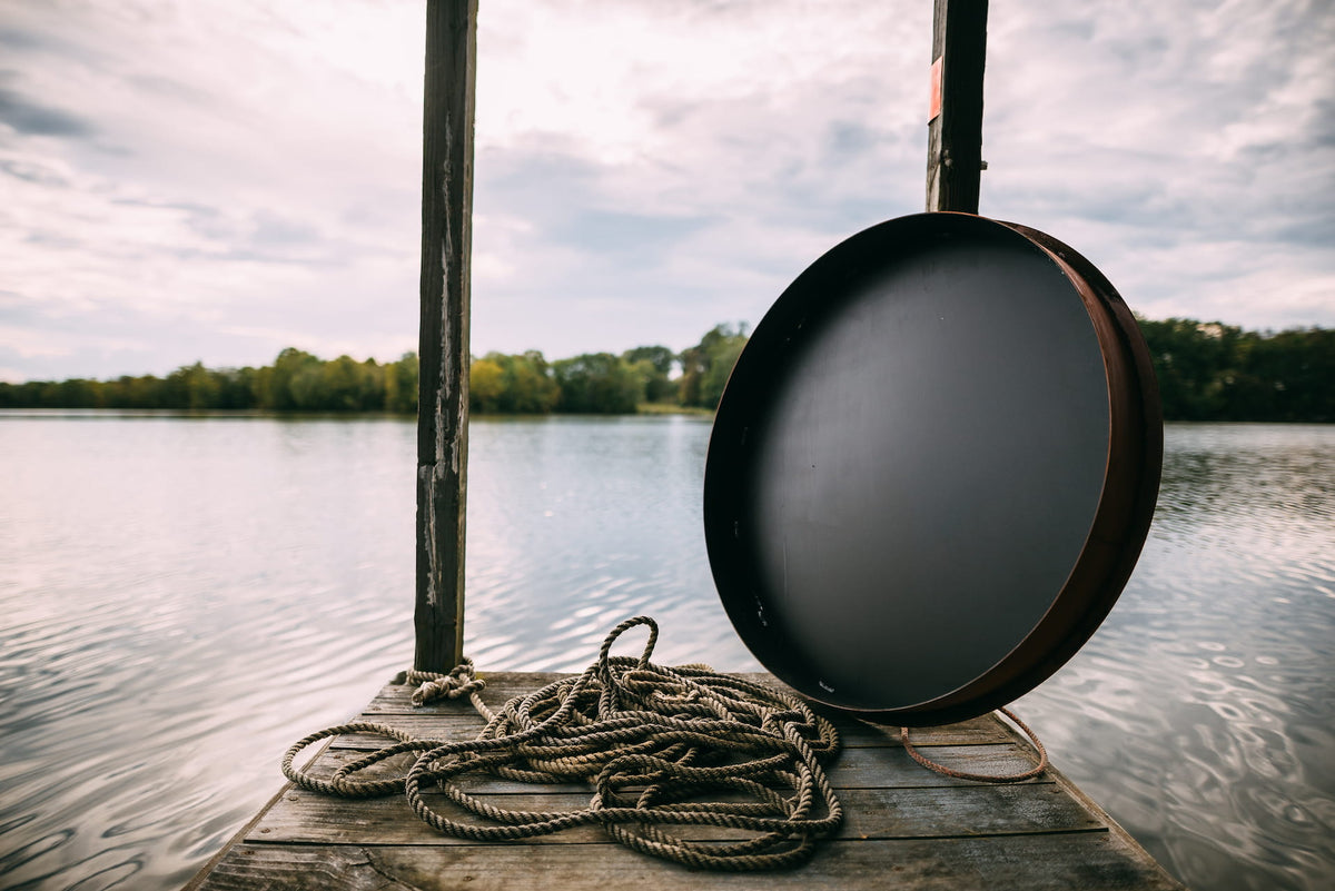 View of black underside to Fire Pit Art’s 40” Carbon Steel Table Top Lid against a lake backdrop.