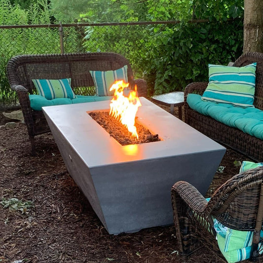 Rectangular Angelus GFRC fire pit in Rustic Grey with natural gas flames glowing on a backyard patio seating area.
