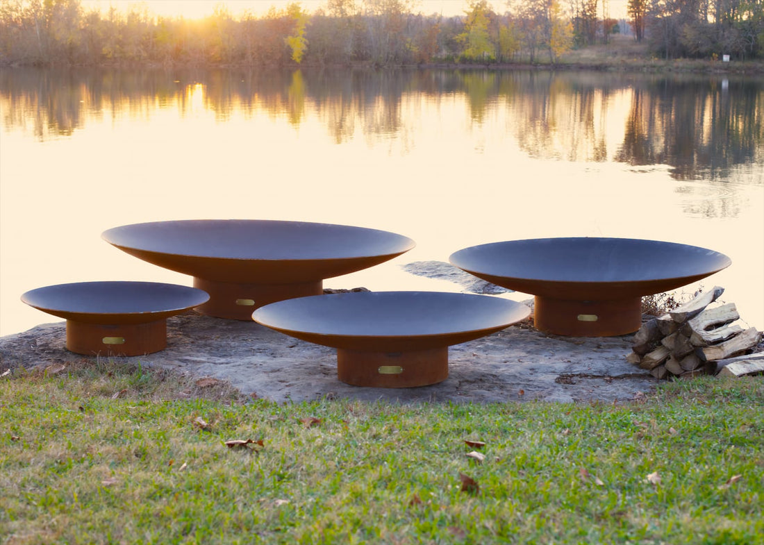 Side profile of all four sizes of the Asia Steel Fire Pit on rocky shore near dock.