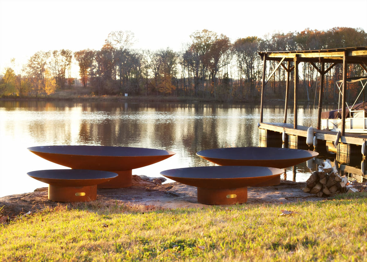 Set of four Asia Carbon Steel Fire Pits displayed next to dock during golden hour.