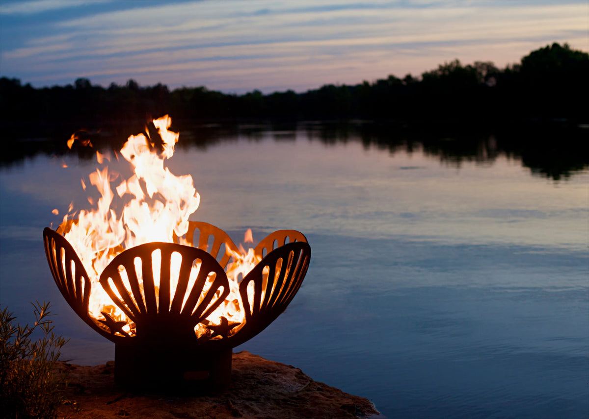 Lit 42" Barefoot Beach Carbon Steel Fire Pit at dusk on lakefront.