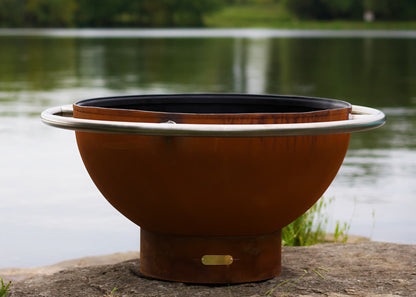 Close-up of stainless steel ring on Bella Luna 48" carbon steel fire pit with lake in the background.  Made in USA by Fire Pit Art. 