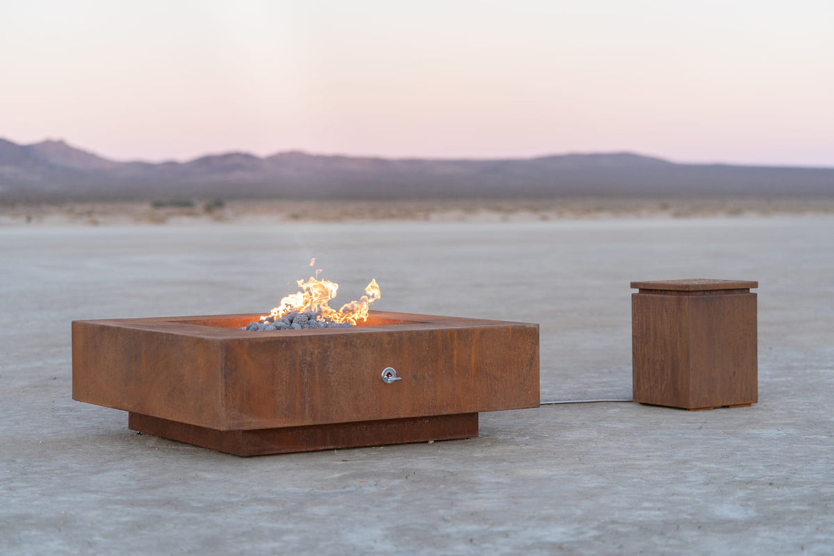 Cabo square corten steel fire pit with propane flame burning in an open desert landscape, paired with a matching propane tank enclosure.