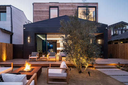Cabo square corten steel fire pit glowing at dusk on a modern patio with warm lighting and outdoor seating.