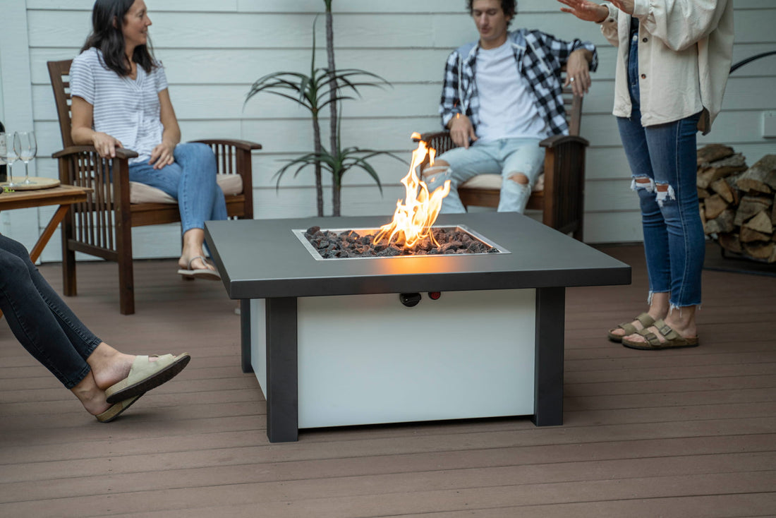 People chatting on patio around Carolina Evening Companion Square fire table lit with gentle flame (shown in Endura Charcoal &amp; White).