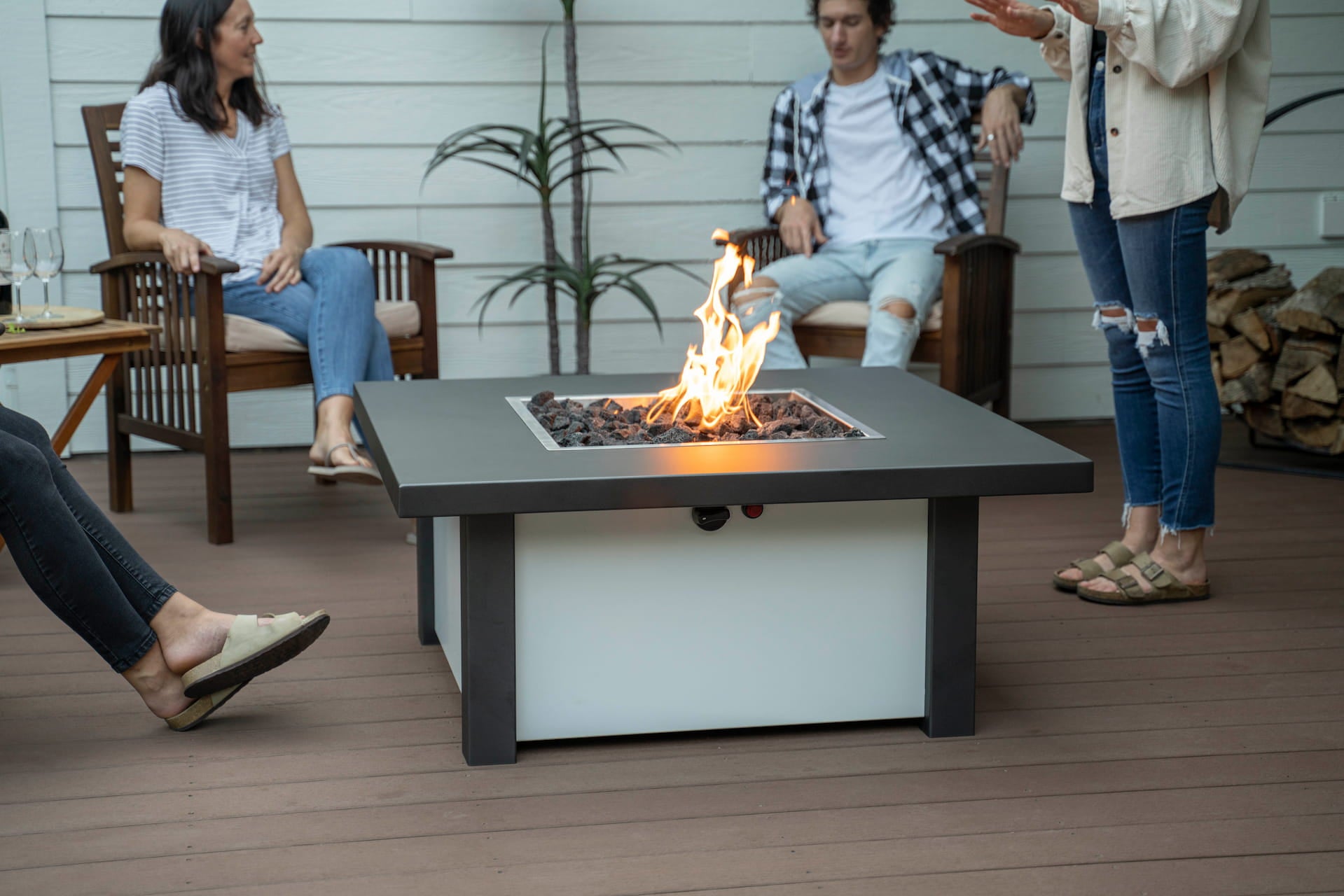 People chatting on patio around Carolina Evening Companion Square fire table lit with gentle flame (shown in Endura Charcoal & White).