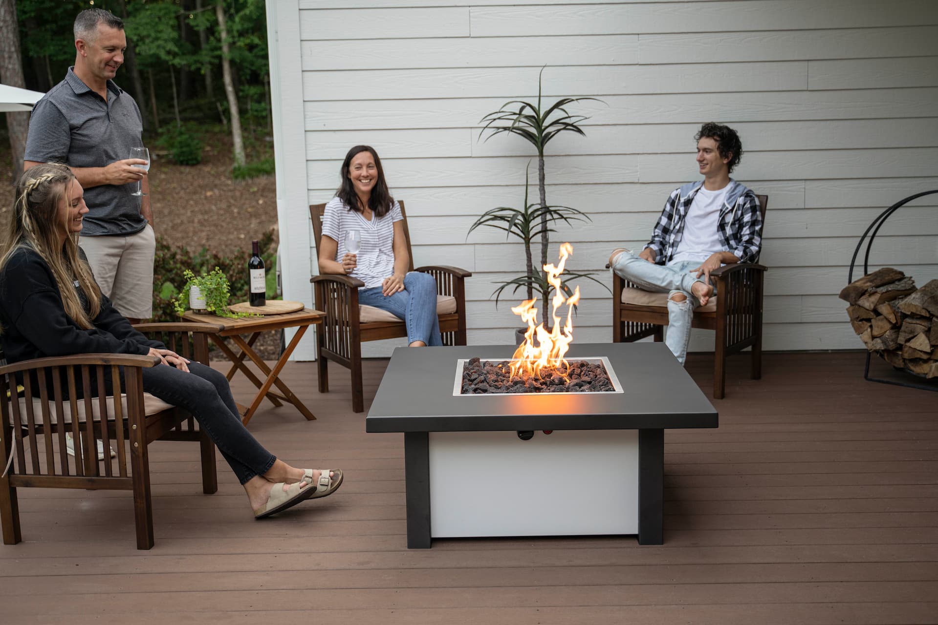 Group of friends gathered around lit Carolina Evening Companion Square fire table enjoying wine and conversation outdoors (table shown in Endura Charcoal and White).