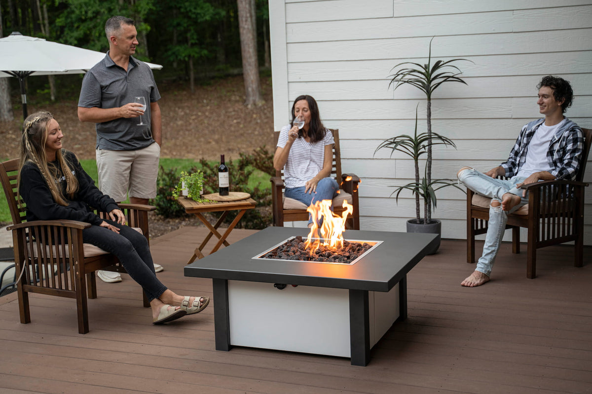Carolina Evening Companion Square fire table with bright flame at center, surrounded by relaxed guests on a wooden deck (shown in Endura Charcoal and White).