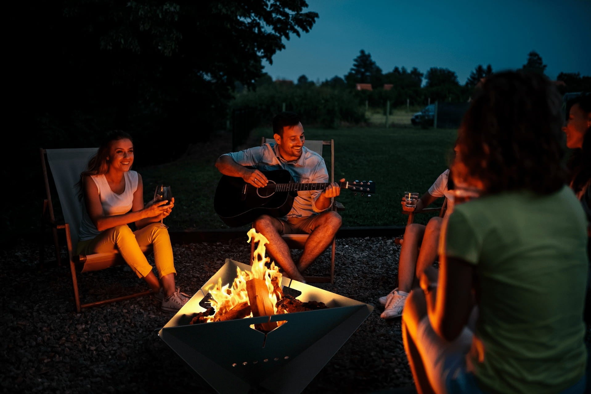 Group of people gathered around The Delta fire pit at night with a campfire burning in the center.