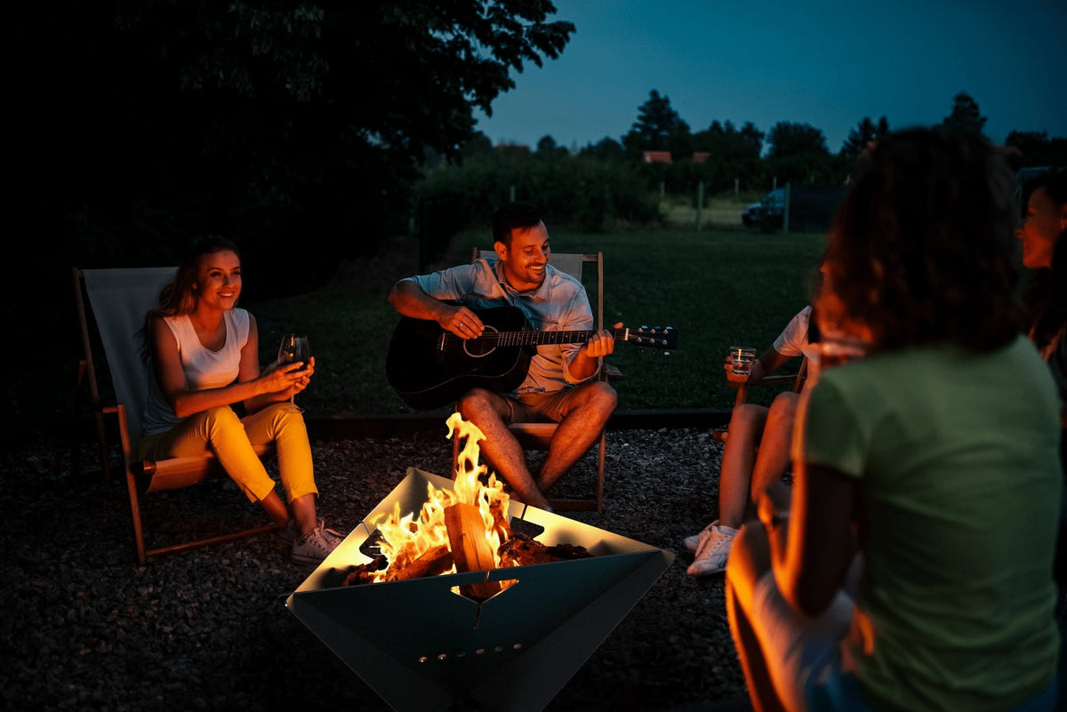 Group of people gathered around The Delta fire pit at night with a campfire burning in the center.