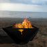 Up close image of steel Delta Fire Pit burning wood with the ocean at dusk in the background.